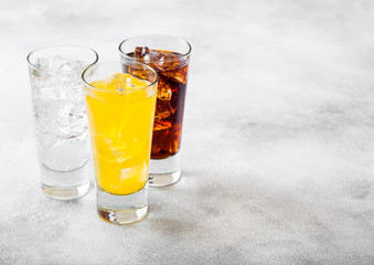Glasses of soda drink with ice cubes and bubbles on stone kitchen table background. Cola and orange...