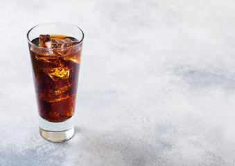 Glass of cola soda drink with ice cubes and bubbles on stone kitchen table background.