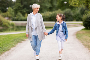 family, leisure and people concept - happy grandmother and granddaughter walking at summer park