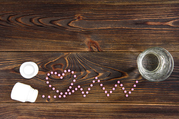 Pills in shape of heart and glass of water on dark wooden background. 