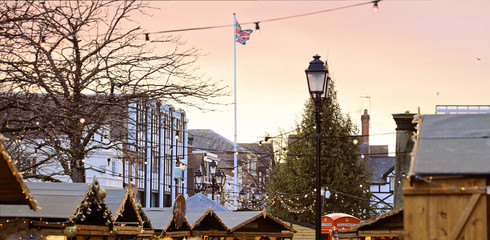 Christmas Market and tree. Stalls decorated with lights. British flag on sunset sky.