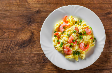 scrambled eggs with shrimp and green onions in white plate on wooden table background.