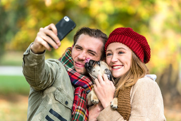 Frau und Mann mit Hund beim Herbst Spaziergang nehmen ein Selfie mit dem Handy auf, Hund schleckt...