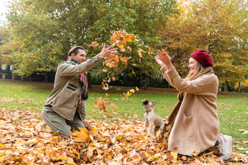 Paar aus Frau und Mann spielt mit ihrem Hund im Herbst