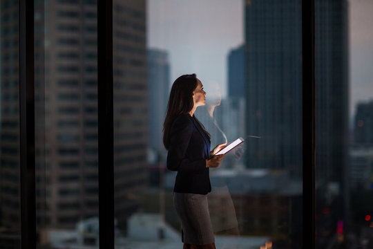 Businesswoman working late using digital tablet with city skyline in background