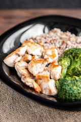 Roasted chicken breast with broccoli and buckwheat porridge on black plate on wooden background.
