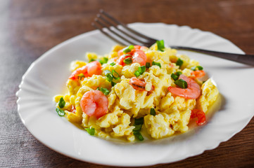 Fototapeta na wymiar scrambled eggs with shrimp and green onions in white plate on wooden table background.