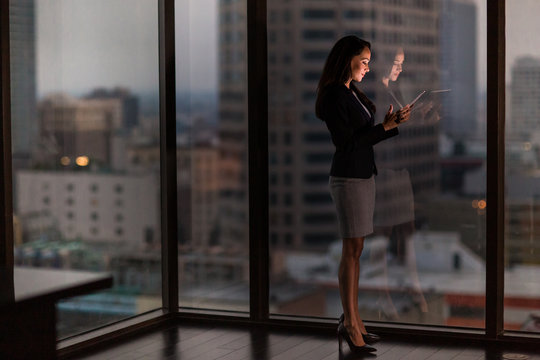 Businesswoman working late using digital tablet with city skyline in background