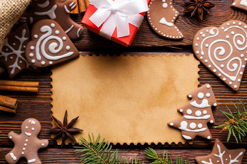 Christmas background - blank paper card, gingerbread cookies, spices and gift box on wooden table