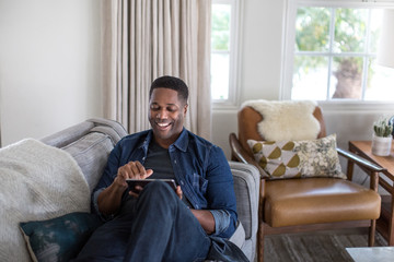 African American adult male using digital tablet at home on sofa