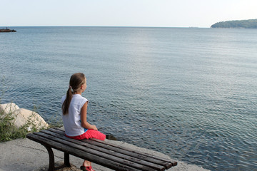 girl looks at the sea sitting on a bench on the beach