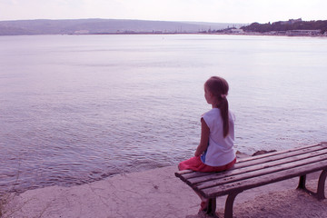 girl looks at the sea sitting on a bench on the beach