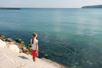 girl stands on the shore and looks at the sea