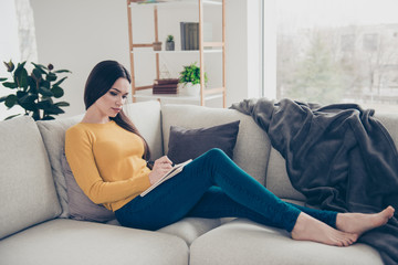 Obraz premium Nice lovely attractive focused girl sitting on divan writing commercial texts textbook in light interior room
