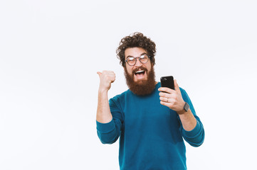 Portrait of cheerful bearded hipster man holding phone and showing thumbs up or pointing away over...