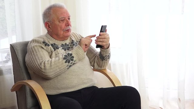 An elderly gray-haired man with a mustache dials a number and talks on the phone