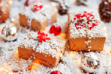 Christmas and New Year background with presents, ribbons, balls and different decorations on snow. Present packed in craft paper with toy fir tree.
