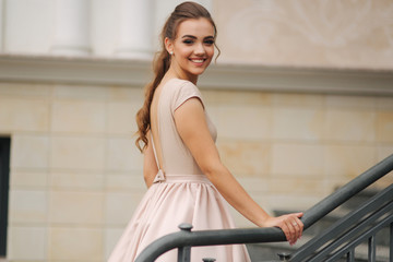 Elegant brunette stand on stairs by the hotel. Fashion model in evening dress