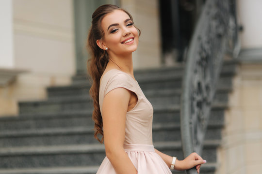 Elegant brunette stand on stairs by the hotel. Fashion model in evening dress