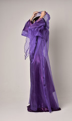 full length portrait of beautiful girl with long black hair,   wearing purple fantasy medieval gown and cloak. standing pose on grey studio background.