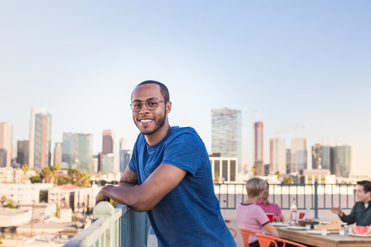 Portrait of young adult male at a rooftop party with city skyline