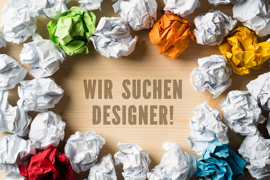 Nachricht "Wir suchen Designer" auf Holzuntergrund, umrandet von vielen zerknüllten Papierkugeln