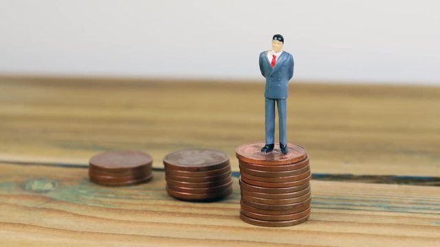 Miniature people standing on piles of coins. Income and economic inequality concept
