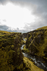 Deep canyon, steep cliffs overgrown with green moss, surrounded by a very fast river with cold water. Canyon of Icelandic tales - Fjardrarglufur