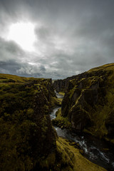 Deep canyon, steep cliffs overgrown with green moss, surrounded by a very fast river with cold water. Canyon of Icelandic tales - Fjardrarglufur