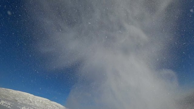 bottom view. rider on a snowmobile flying over the operator. caterpillar close-up. a wave of snow flies beautifully, against the blue sky in a mountain valley. super slow motion video. high quality