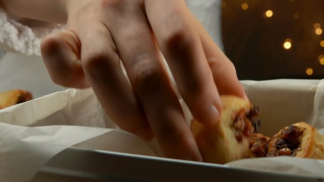 Hand takes Italian Fig Cookies Cucidati from a pan against the background of Christmas light strings, buccellati, traditional sicilian pastry