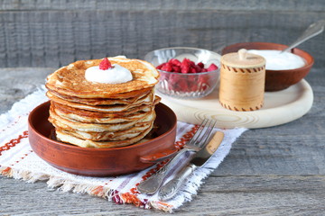A stack of pancakes and a sour cream in a clay bowls on the wooden background.