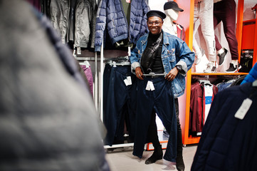 Stylish casual african american man at jeans jacket and black beret at clothes store looking on new sport pants.