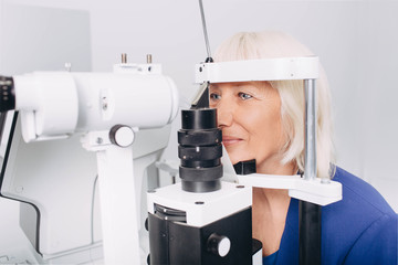 Senior woman checking vision with special eye equipment at doctor office