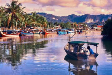 A local fisherman goes out on a boat from boats park to the sea for fishing. Traditional colorful asian fishing boats in fishing village. Langkawi island, Malaysia.