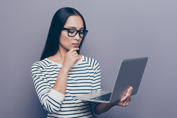 Portrait of nice focused attractive straight-haired lady in striped pullover eyeglasses eyewear holding laptop thinking about e-commerce touching chin isolated on gray pastel background