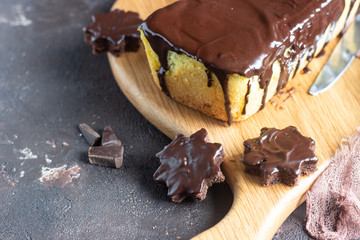 Vanilla pound cake with chocolate glaze served with chocolate biscuit stars on wooden cutting board. Brown stone table. Copy space.