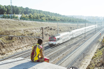 Naklejka premium African businessman sitting next to the railroad with the clothes of typical