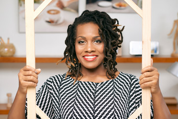Portrait of African businesswoman with dreadlocks looking through a picture frame and smiling