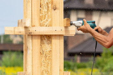 Close up cropped photo of drill instrument in worker hand. He using tool to make hole in wooden pole construction or column formwork
