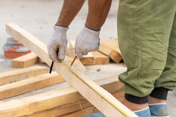 Close up cropped photo of unrecognizable man in white protective gloves on hand holding pencil making mark on plank board using measurement