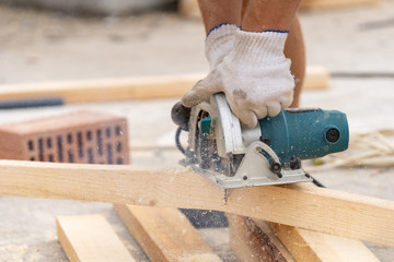 Close up cropped photo of unrecognizable worker using electric saw with sharp blade in hands and cut plank board for special construction or column formwork