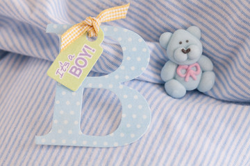 cute striped baby shirt in the background in soft pastel blue with teddy bear made of icing sugar and letter B, perfect for ,baby shower party, Invitation, baptism, birthday, everything around babies