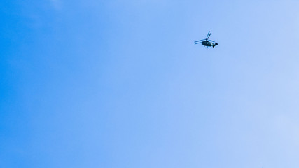 Fototapeta na wymiar small silhouette of a helicopter on a background of clean blue sky. copy space for text