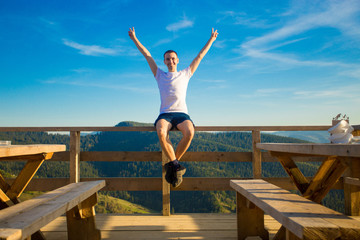 Young man sits in open air cafe with terrace and enjoy beautiful view of mountains