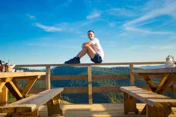 Young man sits in open air cafe with terrace and enjoy beautiful view of mountains