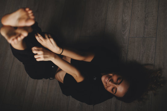 Attractive sexy woman lies on the floor. Girl looks happy and smiles. Woman lying on floor with legs up.