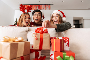 Photo of joyful people looking at present boxes, while celebrating Christmas in apartment