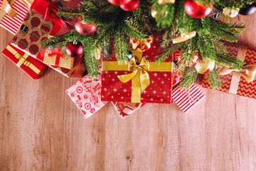 Top view composition of Christmas tree branches with stack of different presents in colorful festive wrapping tied with bow. Pile of gifts under spruce tree on wooden floor. Background, copy space.