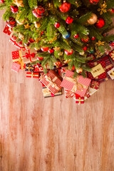 Top view composition of Christmas tree branches with stack of different presents in colorful festive wrapping tied with bow. Pile of gifts under spruce tree on wooden floor. Background, copy space.